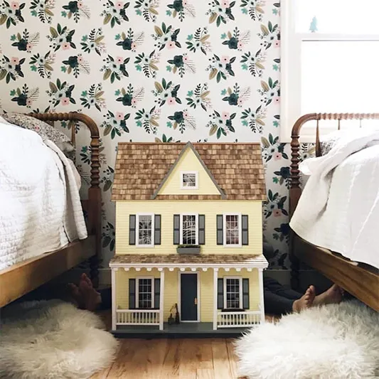 Dollhouse between two beds with floral wallpaper.